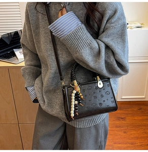 Detail of black crossbody bag featuring embossed puppy patterns and beaded handle charm