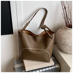 Detail of brown litchi pattern bucket bag with white piping and knotted handle design