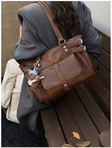Detail of vintage brown leather tote bag with pocket and cute plush bear charm on a bench