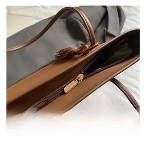 Close-up of golden metal zipper and tassel detail on brown leather tote bag