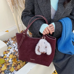Detail der weinroten Shopper-Tasche mit weißen Kontrastnähten und Plüsch-Hasen-Anhänger
