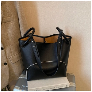 Detail of black pebble leather bucket bag with contrast piping and dual strap design