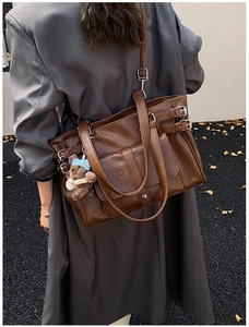 Brown vintage faux leather tote bag with metal buckles styled on a grey coat outdoors