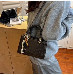 Detail of dark brown glossy embossed tote bag with braided handles and beaded charm