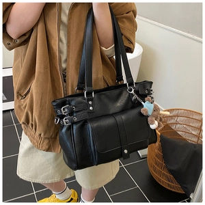 Detail of a black large tote bag featuring front flap pocket and a cute bear charm accessory