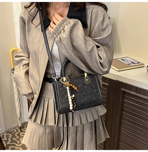 Detail of black embossed leather handbag featuring woven handles and beaded charm accessory