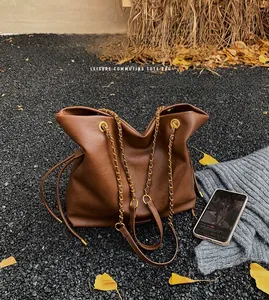Macro shot of a brown leather bucket tote bag with gold chain strap on pebbles