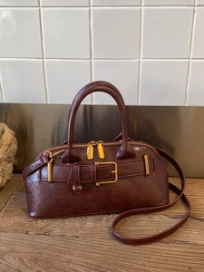 Minimalist burgundy leather handbag with golden buckle on a rustic wooden table