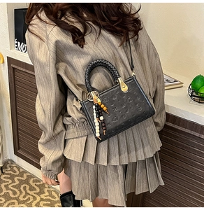 Black leather handbag with woven handle and bead charm shown on model's shoulder
