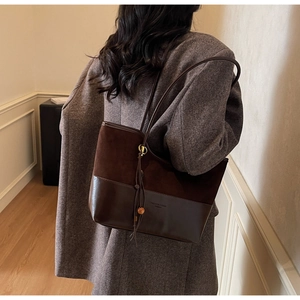 Detail of dark brown tote bag with suede texture and decorative tassel on a model