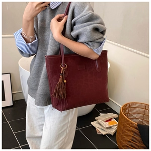 Detail of burgundy tote bag with subtle leopard texture and detachable leather tassel