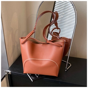 Detail of a brown leather bucket bag with white trim on a sleek dark surface