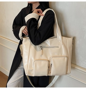 Cream-colored large tote bag shown on shoulder featuring two front zipper pockets