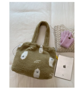 Dettaglio borsa tote in peluche verde muschio con fantasmi accanto a un tablet