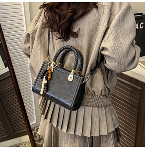Detail of black crossbody bag with embossed bear pattern and beaded charm on model