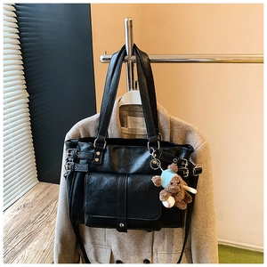 Close-up of black retro tote bag with metal rivets, buckles, and a cute plush bear charm