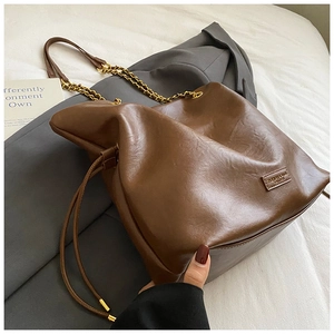 Detail of brown leather bucket bag featuring gold chain strap and side drawstring accents