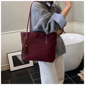 Detail of burgundy leopard embossed tote bag with tassel and brand leather patch