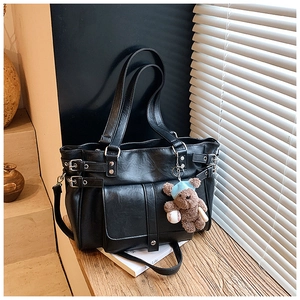 Detail of a black faux leather tote bag with a brown teddy bear charm and adjustable straps
