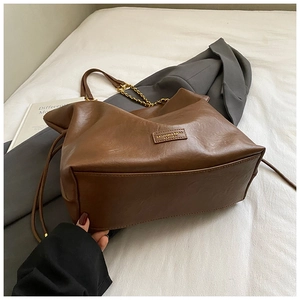 Brown soft leather tote bag detail with fashion label and golden chain strap on white linen