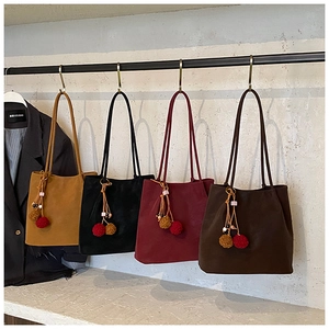 Detail of four colorful suede tote bags with plush pendants on a minimalist metal rack
