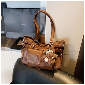Detail of a brown vintage tote bag with metal buckles and a cute plush bear charm