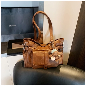 Brown leather tote bag detail with metal buckle and plush bear charm on a soft seat