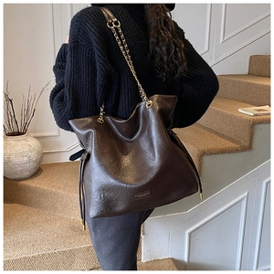 Detail of a large brown textured leather bucket bag with chain strap and side drawstring