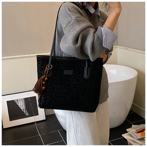 Detail of black leopard print tote bag with brown tassel charm and brand nameplate