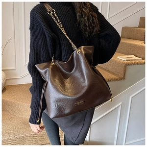 Close-up of brown leather bucket bag with gold chain strap worn by a model in black