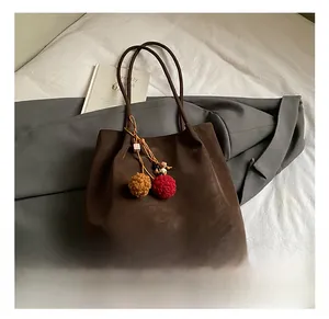 Detail of dark brown suede tote bag with colorful pom-pom charm and rustic texture