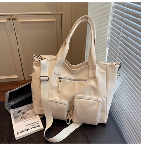 Detail of a cream PU leather tote bag featuring multiple functional zipper pockets