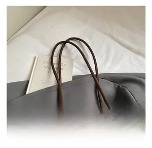 Detail of dark brown suede tote bag with woven fringe charm and slender handles