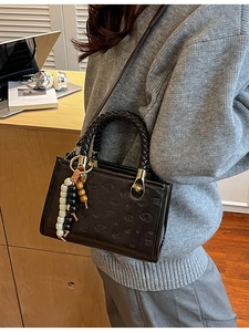 Black embossed rectangular handbag with bear patterns and beaded charm shown on model