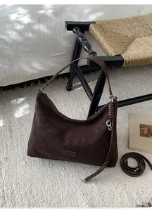 Détail d'un sac cabas Hobo en daim marron foncé avec écusson en cuir et bandoulières