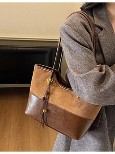 Brown patchwork suede and leather tote bag with fringe charm worn by a model