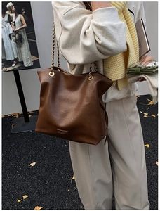 Detail of a large brown tote bag with leather texture and golden chain strap on a model