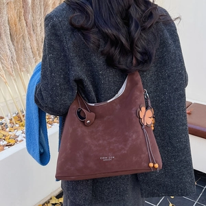 Close-up of brown suede hobo bag with floral charm and wood bead tassels in autumn setting