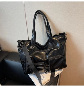 Detail of black washed leather tote bag showing front zipper pockets and wide shoulder strap