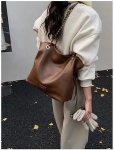 Close-up of brown vintage leather bucket bag with gold chain strap on autumn leaves