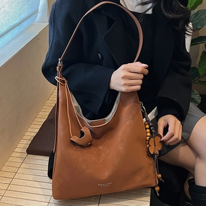 Detailed shot of brown vintage tote bag featuring floral charm and metal brand logo