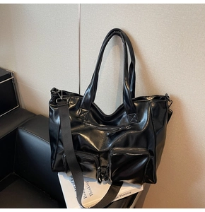 Detail view of black washed PU leather tote bag with functional zippers on a chair