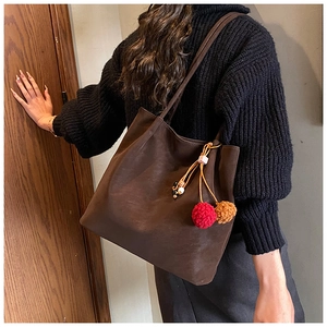 Close-up of brown suede tote bag with colorful pompom charm on a black sweater