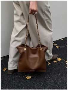 Close-up of a large dark brown leather bucket bag with gold chain strap detail