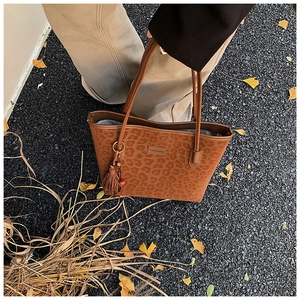 Detail view of leopard print tote bag with brown tassels and autumn foliage background