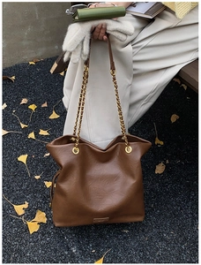 Close-up of brown faux leather bucket bag with gold chain strap and autumn ginkgo leaves
