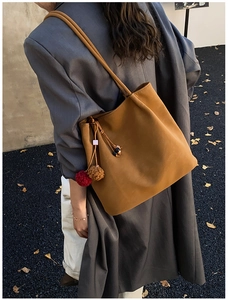 Detail of caramel suede tote bag with plush charm accessory worn with autumn outfit