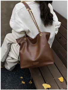 Detailed view of dark brown leather bucket bag with chain strap and brand nameplate
