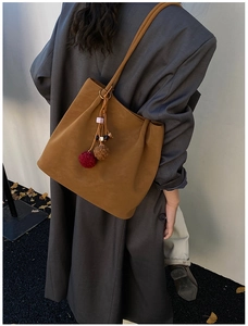 Brown suede tote bag with decorative pompoms worn over a grey oversized blazer