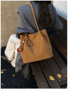 Detail of camel suede tote bag with fringe charm on shoulder of model in autumn setting